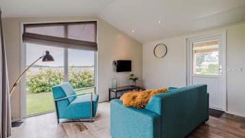 A modern living room with a sofa, a chair, a TV, and a large window offering a view of greenery.