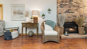 A cozy living room with a brick fireplace, wicker furniture, and a decorative lamp. - Higgins Lake Private Beachfront Home w/Dock, Boat Mooring, Sunset & Sunrise View (Roscommon)