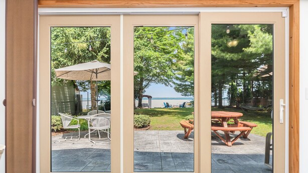A sliding glass door with a view of an outdoor patio area featuring a table and chairs, a hammock, and a view of the lake. - Higgins Lake Private Beachfront Home w/Dock, Boat Mooring, Sunset & Sunrise View (Roscommon)