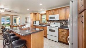 A modern kitchen with wooden cabinets, a granite countertop, and a central island with bar stools. - Higgins Lake Private Beachfront Home w/Dock, Boat Mooring, Sunset & Sunrise View (Roscommon)