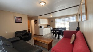 A living room with a red sofa, black leather couch, and a wooden coffee table. There is a kitchen area with white cabinets and a dining table with chairs.