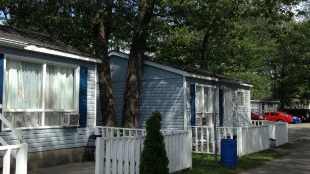 A row of mobile homes with white railings, a small tree, and a blue barrel.