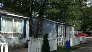 Une rangée de maisons mobiles avec des balustrades blanches, un petit arbre et un baril bleu.
