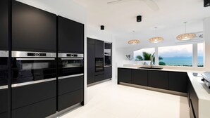 A modern kitchen with black cabinetry, stainless steel appliances, and a view of the ocean. - Villa Murano 9BR with Panoramic Sea View (Koh Samui)