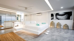 A modern bedroom with a bed, a large mirror, a ceiling fan, and a view of the sea.