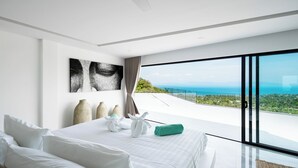 A modern bedroom with a large bed, a view of the ocean, and a painting on the wall. - Villa Murano 9BR with Panoramic Sea View (Koh Samui)