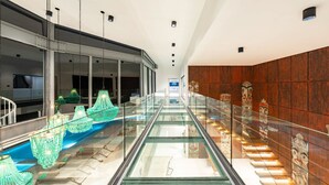 A modern interior with a glass escalator, metal railings, and a wooden wall with tribal art. - Villa Murano 9BR with Panoramic Sea View (Koh Samui)