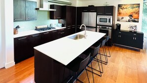 A modern kitchen with a central island, dark cabinetry, and stainless steel appliances. - Private luxury — Minutes from City Center & airport (Austin)