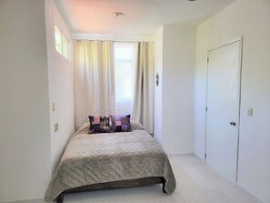 A narrow room with a bed, a window with curtains, and a door. - Furnished upstairs apartment ideally located in Oaxaca's Historical District (Oaxaca de Juárez)