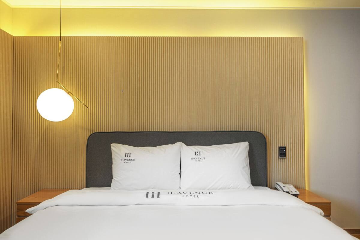A hotel room with a bed, two pillows with the hotel logo, a bedside table with a phone, and a wall with vertical paneling.