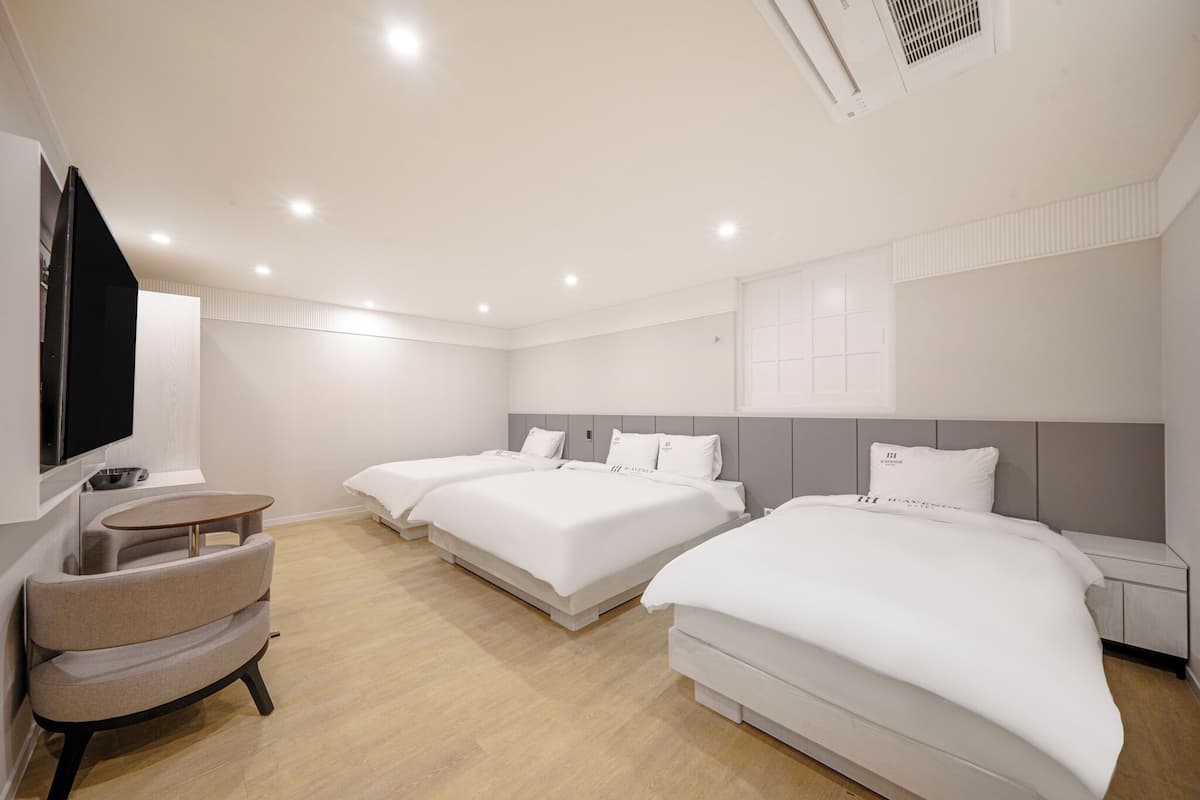 A hotel room with three beds, a TV, a small round table, and a chair.