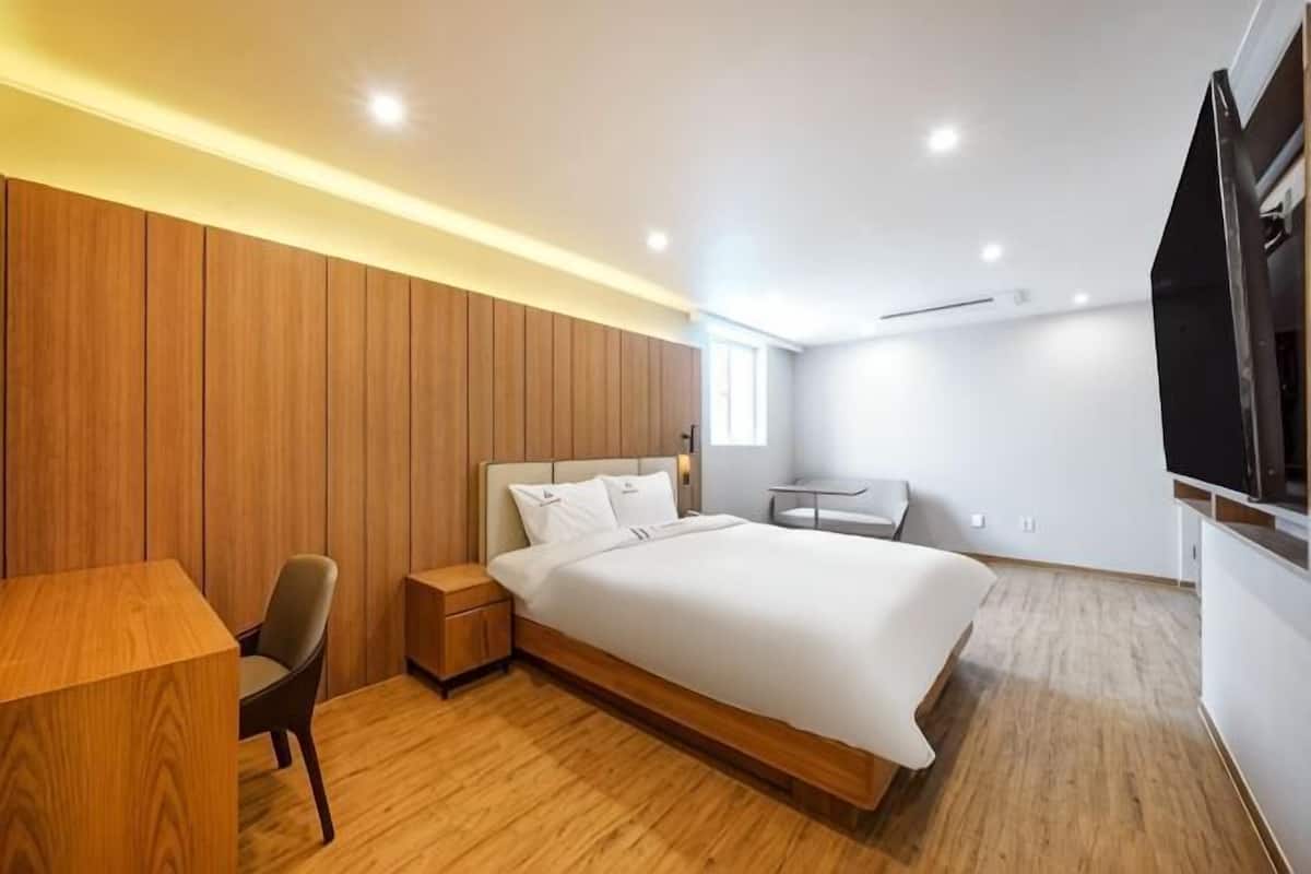 A modern bedroom with a wooden panel wall, a large bed, a desk, and a TV.