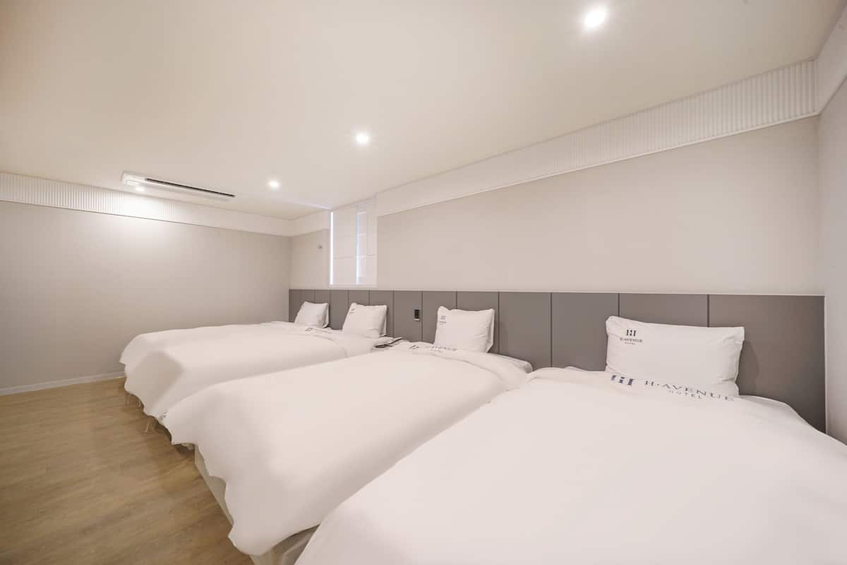 A hotel room with three beds, a wooden floor, and a modern design.
