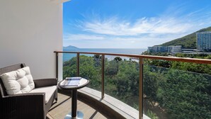 A balcony with a wicker sofa and a small table, overlooking a lush green landscape and a clear blue sky.