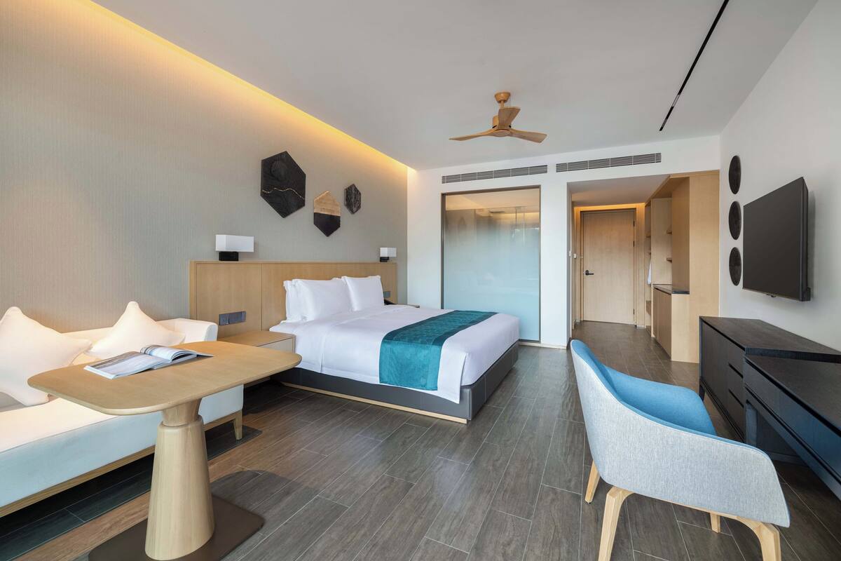 Een moderne hotelkamer met een bed, een bank, een bureau, een stoel, een televisie en een plafondventilator.