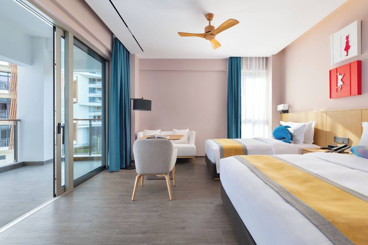 Hotelkamer met een bed, bureau, stoel, plafondventilator en groot raam.