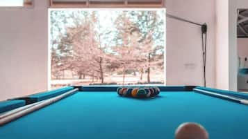 A pool table with a cue ball, a striped cushion, and a window view of trees.