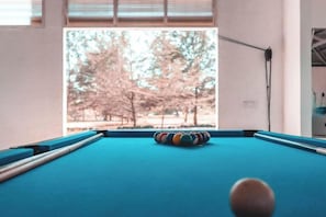 A pool table with a cue ball, a striped cushion, and a window view of trees. - Ara Dinawan Island Resort (Kinarut)