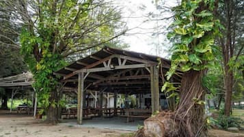 A covered picnic area with benches and tables, surrounded by trees.