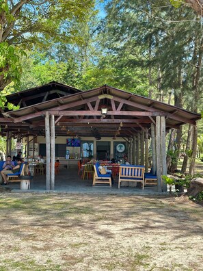 Un espacio exterior con mesas y sillas, un pabellón cubierto y vistas al bosque circundante.