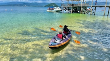 Um caiaque em águas calmas, com um cais e um barco ao fundo.