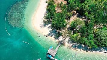 Vue aérienne d’une plage avec un quai, des eaux turquoise et limpides, et une végétation luxuriante.