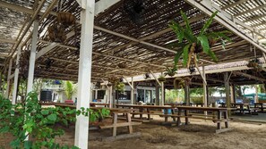 An outdoor covered area with wooden benches, hanging plants, and a water tank. - Ara Dinawan Island (Kinarut)