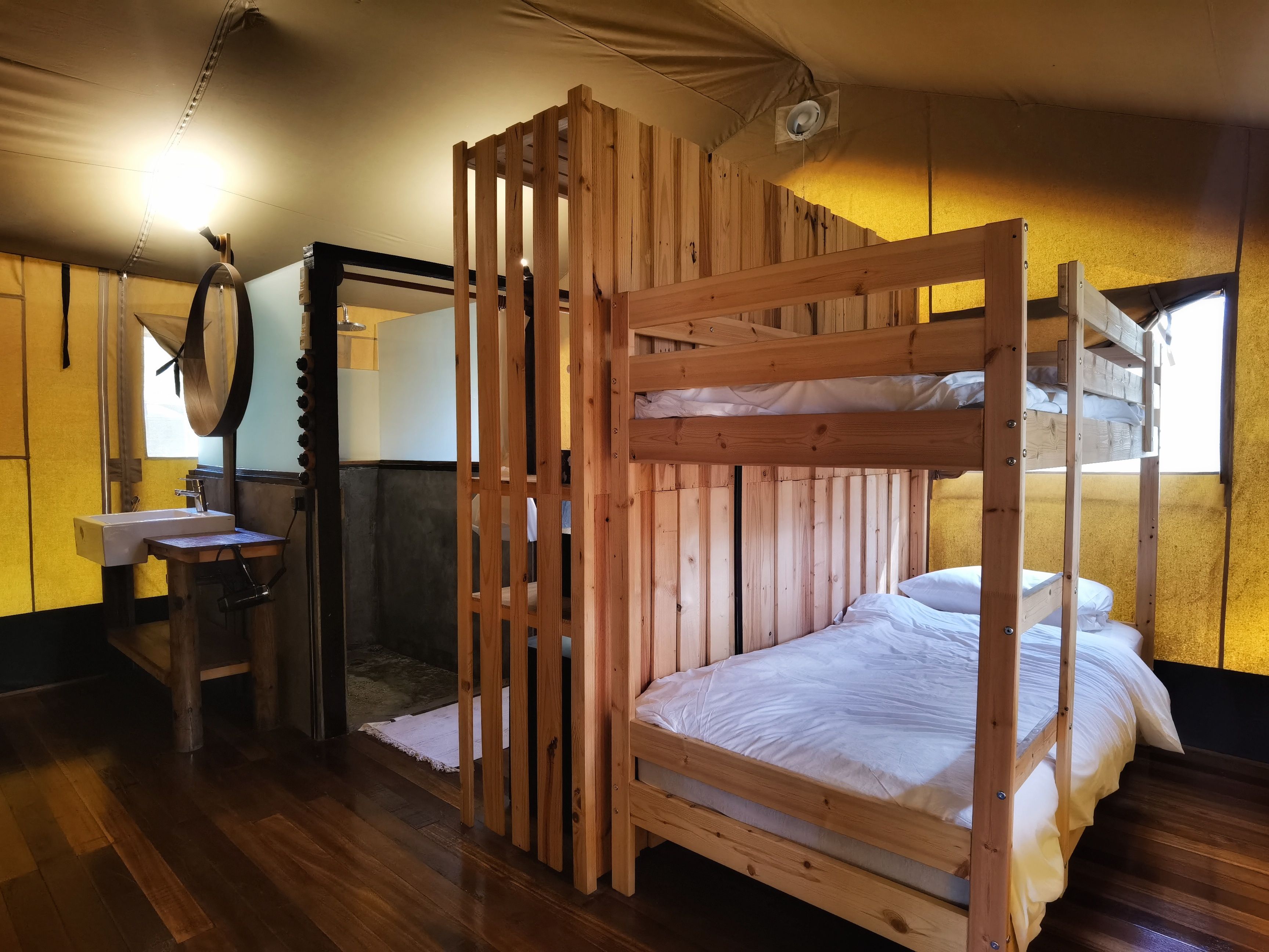 A bunk bed room with a wooden floor, a sink, and a mirror.