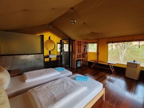 Une chambre avec deux lits, une table en bois, un lavabo et une fenêtre donnant sur des arbres.