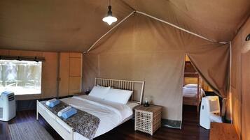 A tented room with a bed, a small bedside table, a heater, and a window.