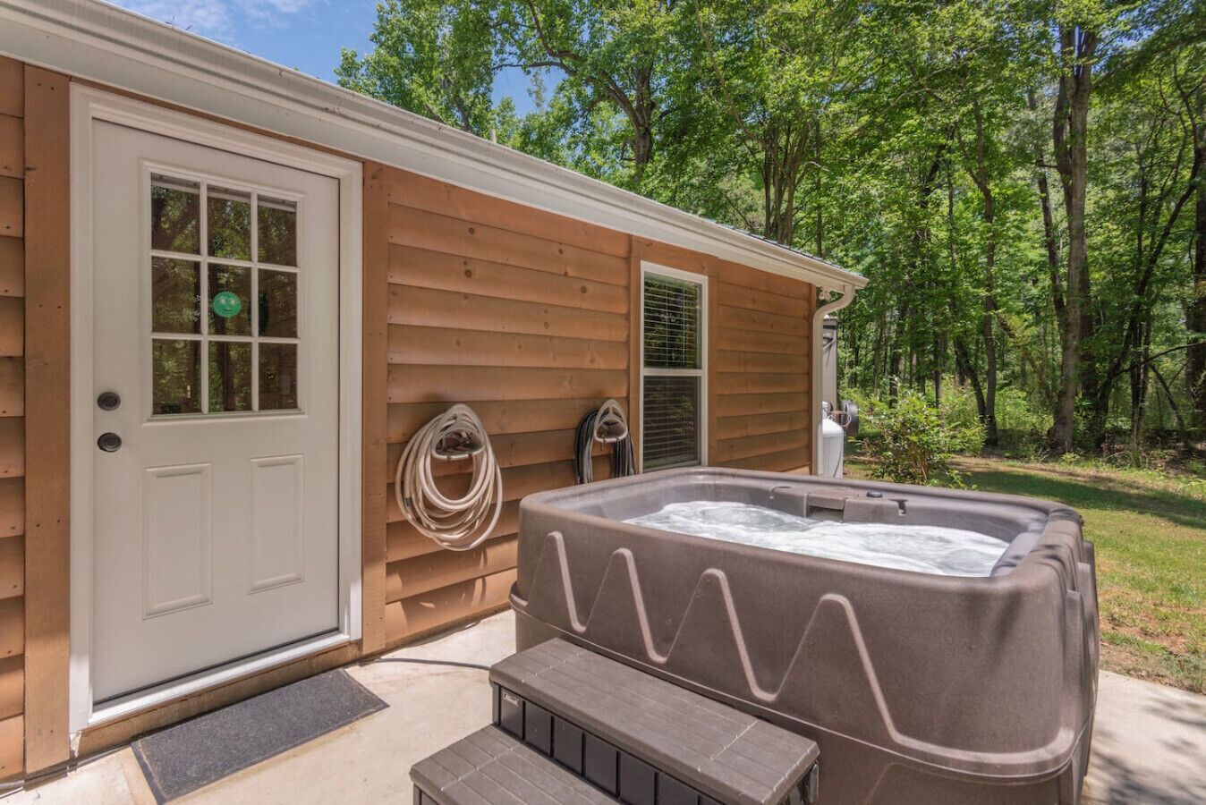 Une cabane en bois avec un jacuzzi, une porte et une fenêtre.