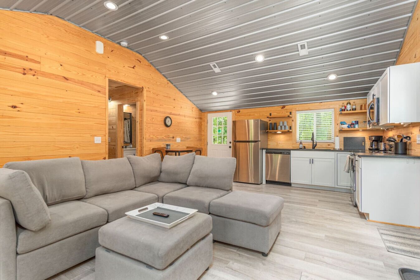 Un intérieur moderne de chalet en bois, avec un canapé d’angle, une cuisine équipée d’appareils électroménagers en acier inoxydable et un plafond en bois.