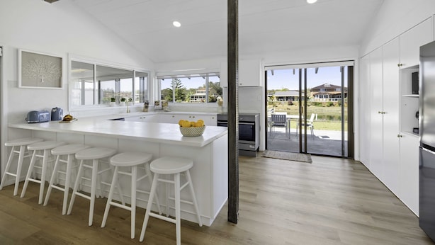 A modern kitchen with a large island, bar stools, and a view of the outdoors. - Deja Bleu - family home with private jetty (Port Macquarie)