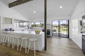 A modern kitchen with a large island, bar stools, and a view of the outdoors. - Deja Bleu - family home with private jetty (Port Macquarie)