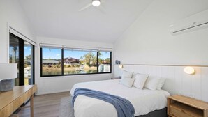 A modern bedroom with a large bed, a desk, and a view of a lake and houses. - Deja Bleu - family home with private jetty (Port Macquarie)