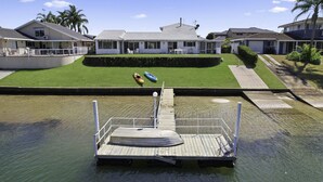 A dock with a boat and a rowboat, a grassy area with a house, and a clear sky. - Deja Bleu - family home with private jetty (Port Macquarie)