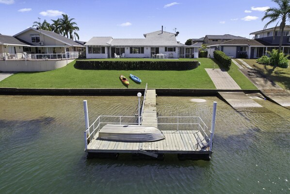 A dock with a boat and a rowboat, a grassy area with a house, and a clear sky. - Deja Bleu - family home with private jetty (Port Macquarie)