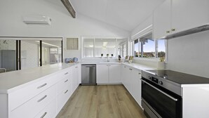 A modern kitchen with white cabinetry, a stainless steel dishwasher, and a built-in oven. - Deja Bleu - family home with private jetty (Port Macquarie)