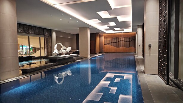A modern indoor swimming pool with a geometric tile design, surrounded by contemporary decor and a long corridor. - Branz Apartment BSD City by Nagisa Bali (Pagedangan)