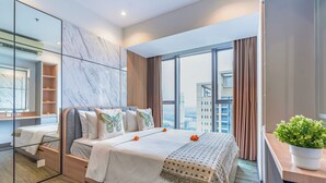 A modern hotel room with a large bed, a desk, and a large window offering a city view. - Branz Apartment BSD City by Nagisa Bali (Pagedangan)