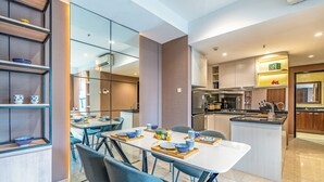 A modern kitchen with a central island, built-in shelves, and a dining area with a white table and blue chairs. - Branz Apartment BSD City by Nagisa Bali (Pagedangan)