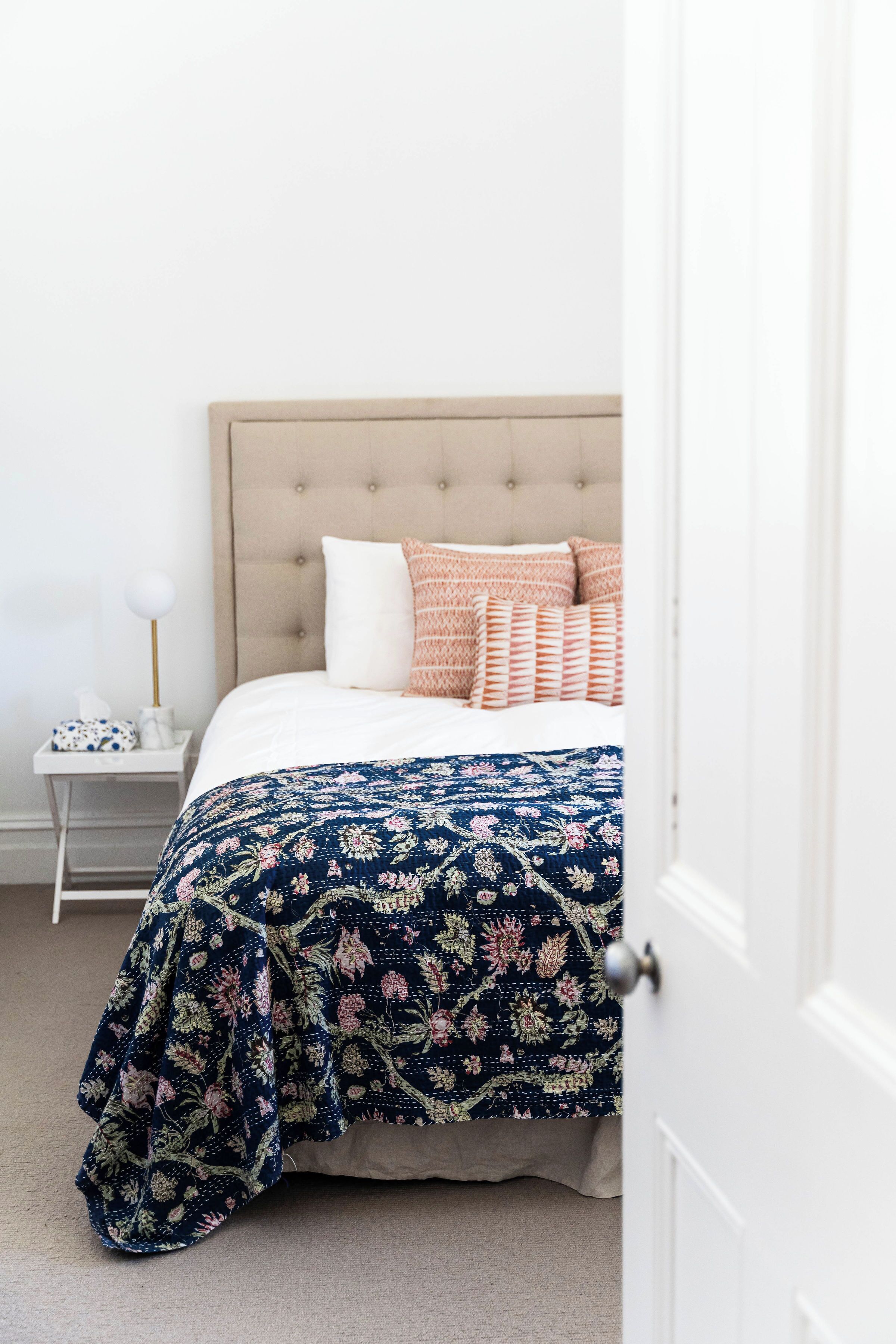 A bedroom with a tufted headboard, a floral-patterned bedspread, and a bedside table with a lamp.