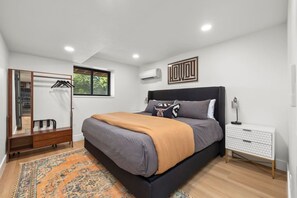 Une chambre moderne avec un grand lit, une armoire, une table de chevet et une fenêtre donnant sur un paysage verdoyant.