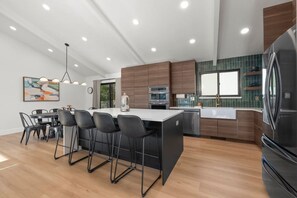 Una cocina moderna con una isla central, taburetes de bar, zona de comedor y un refrigerador grande.
