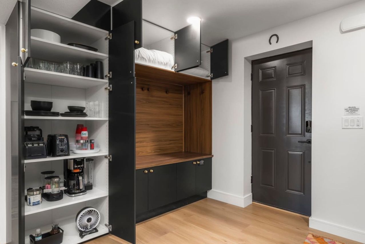 Een kleine keuken met inbouwapparatuur, een houten plank en een donkere deur.