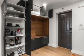 Une cuisine compacte dotée d’appareils électroménagers intégrés, d’une étagère en bois et d’une porte sombre.