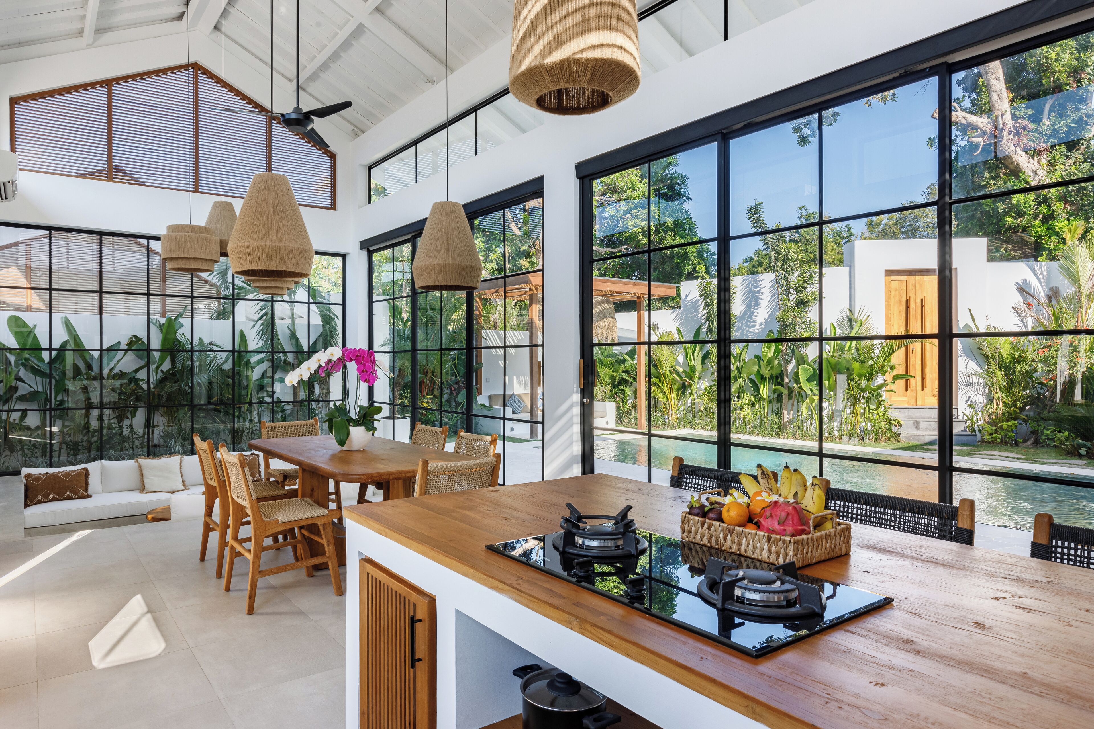 Une cuisine moderne avec un îlot central en bois, de grandes fenêtres et une vue sur une piscine et un espace verdoyant.