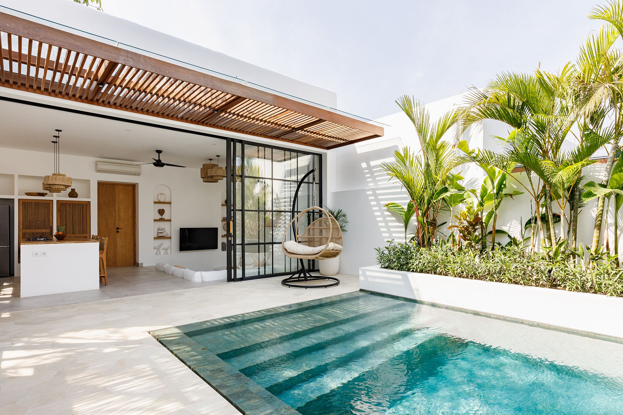 Ein modernes Haus mit Swimmingpool, einer Holz-Pergola und tropischen Pflanzen.