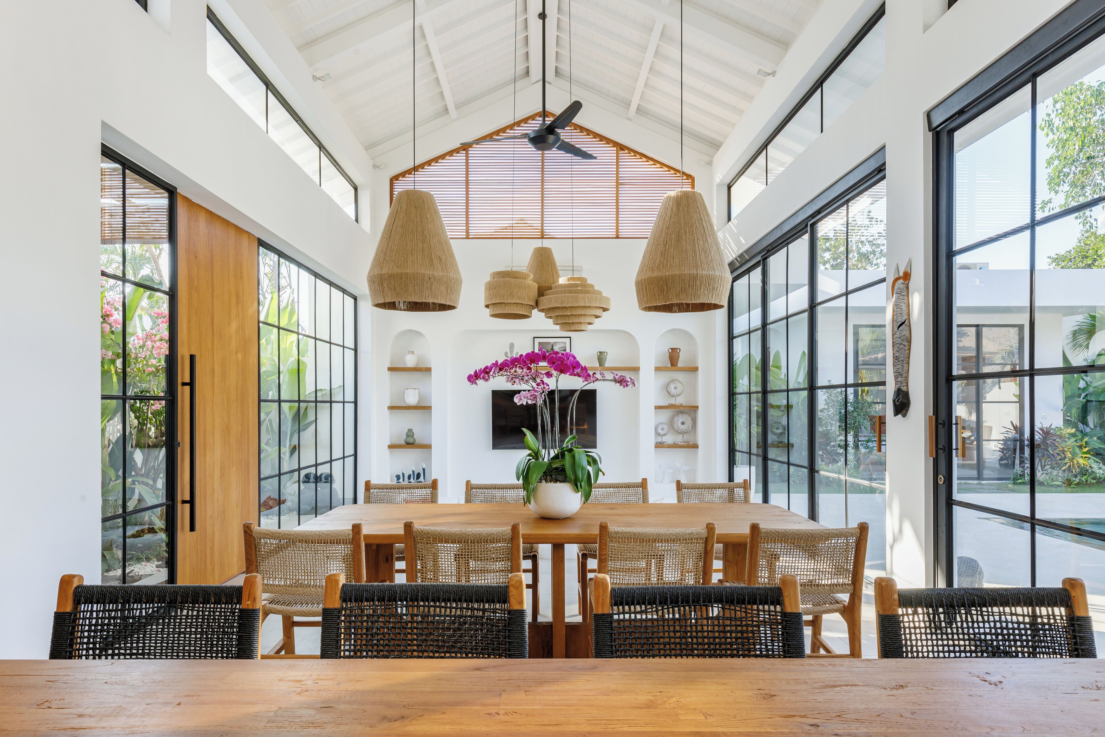 A spacious dining area with a large wooden table, woven chairs, and pendant lights.