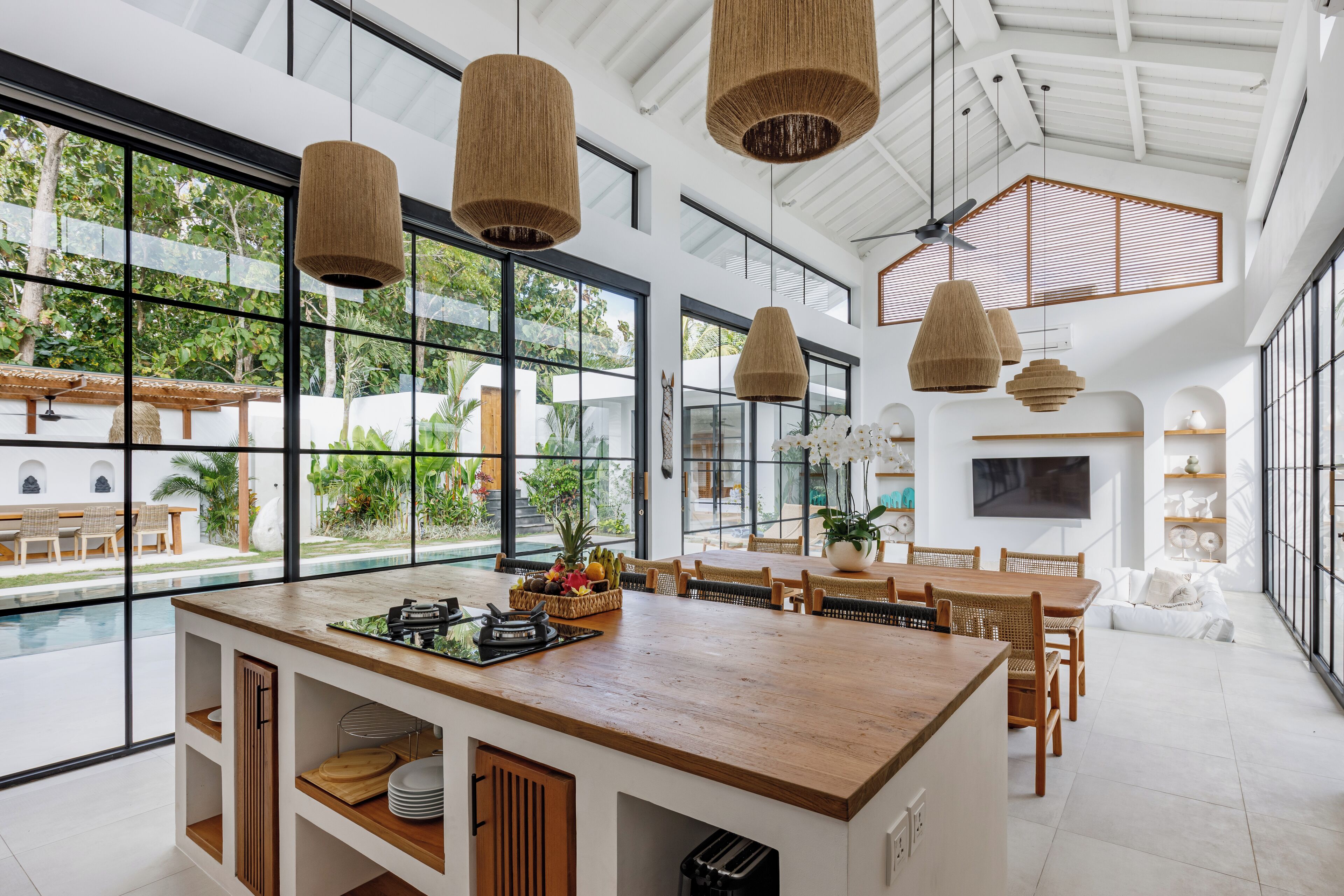 A spacious dining area with a wooden table and chairs, large windows, and hanging wicker lamps.